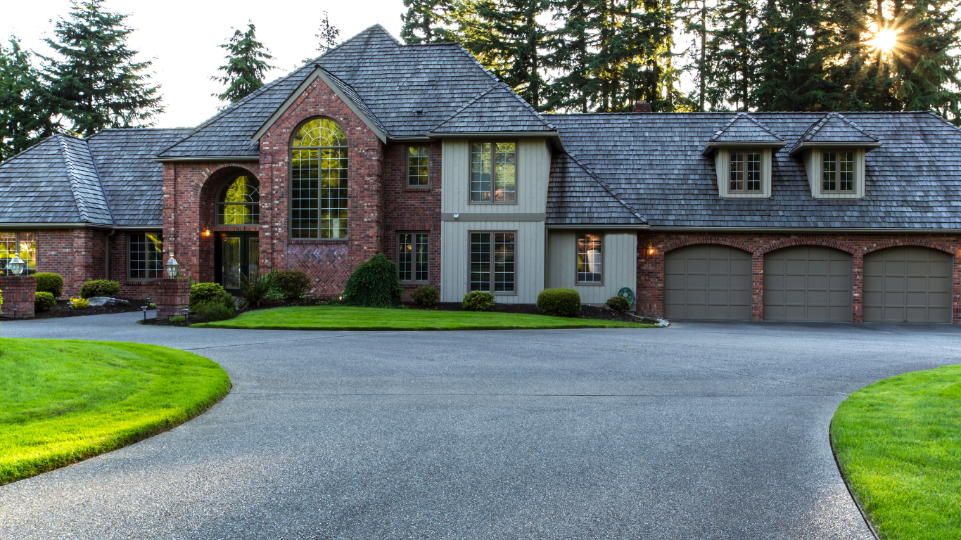 A large brick house with three garage doors and a driveway leading to it.