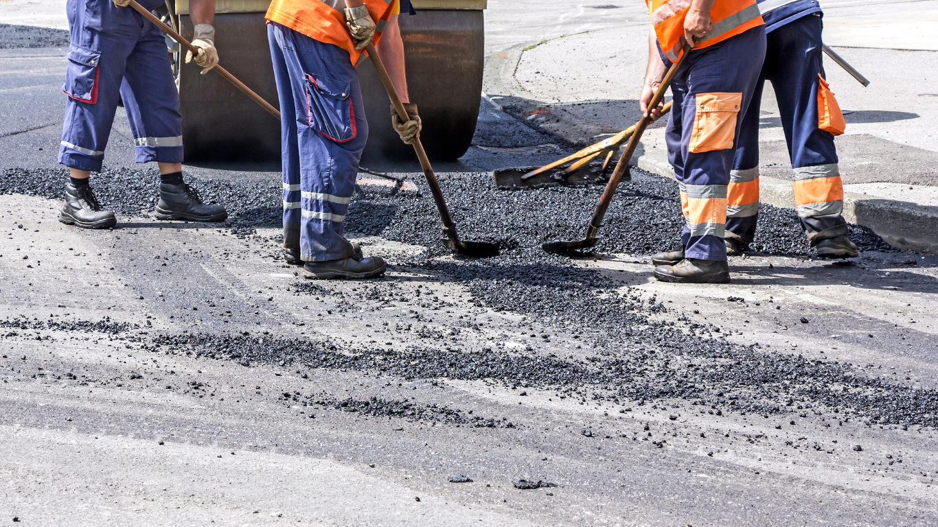 A group of construction workers are working on a road doing asphalt repair.