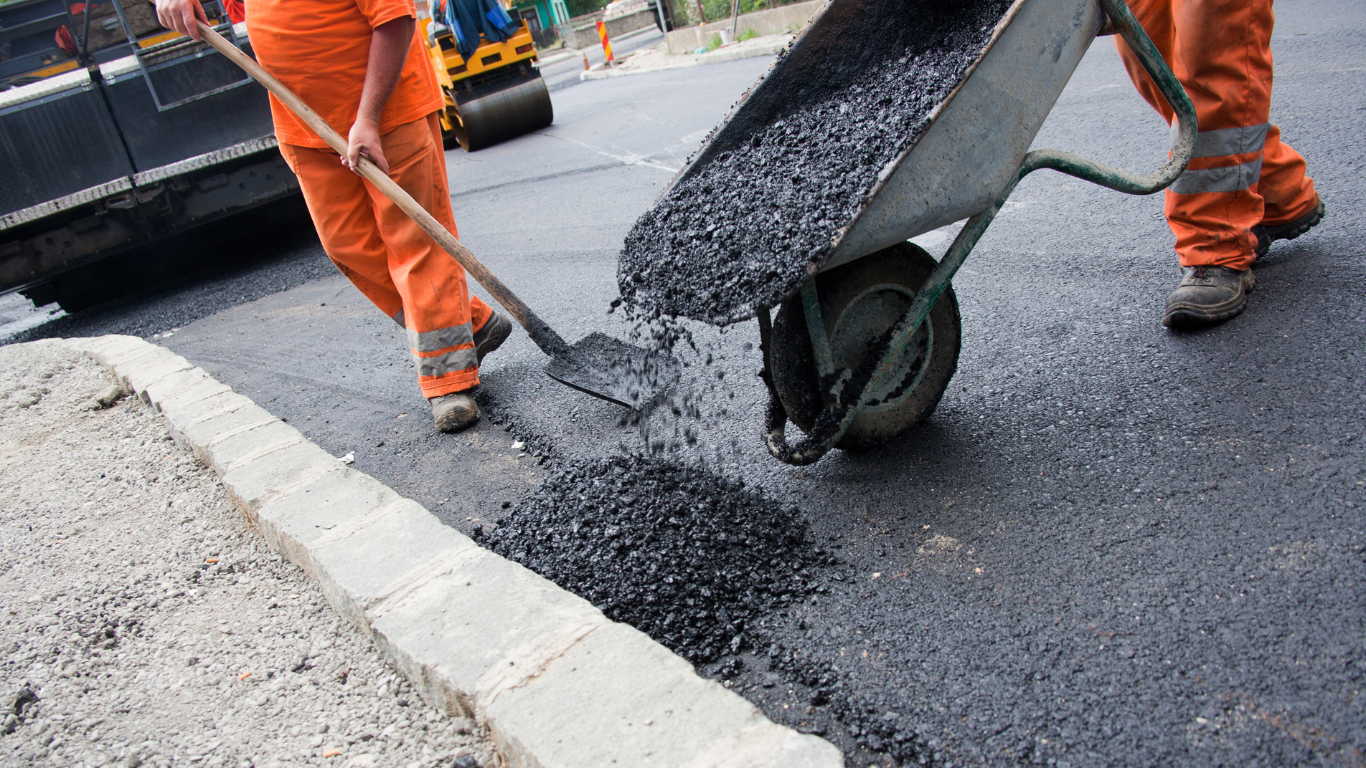 A man is pushing a wheelbarrow full of asphalt for asphalt repair