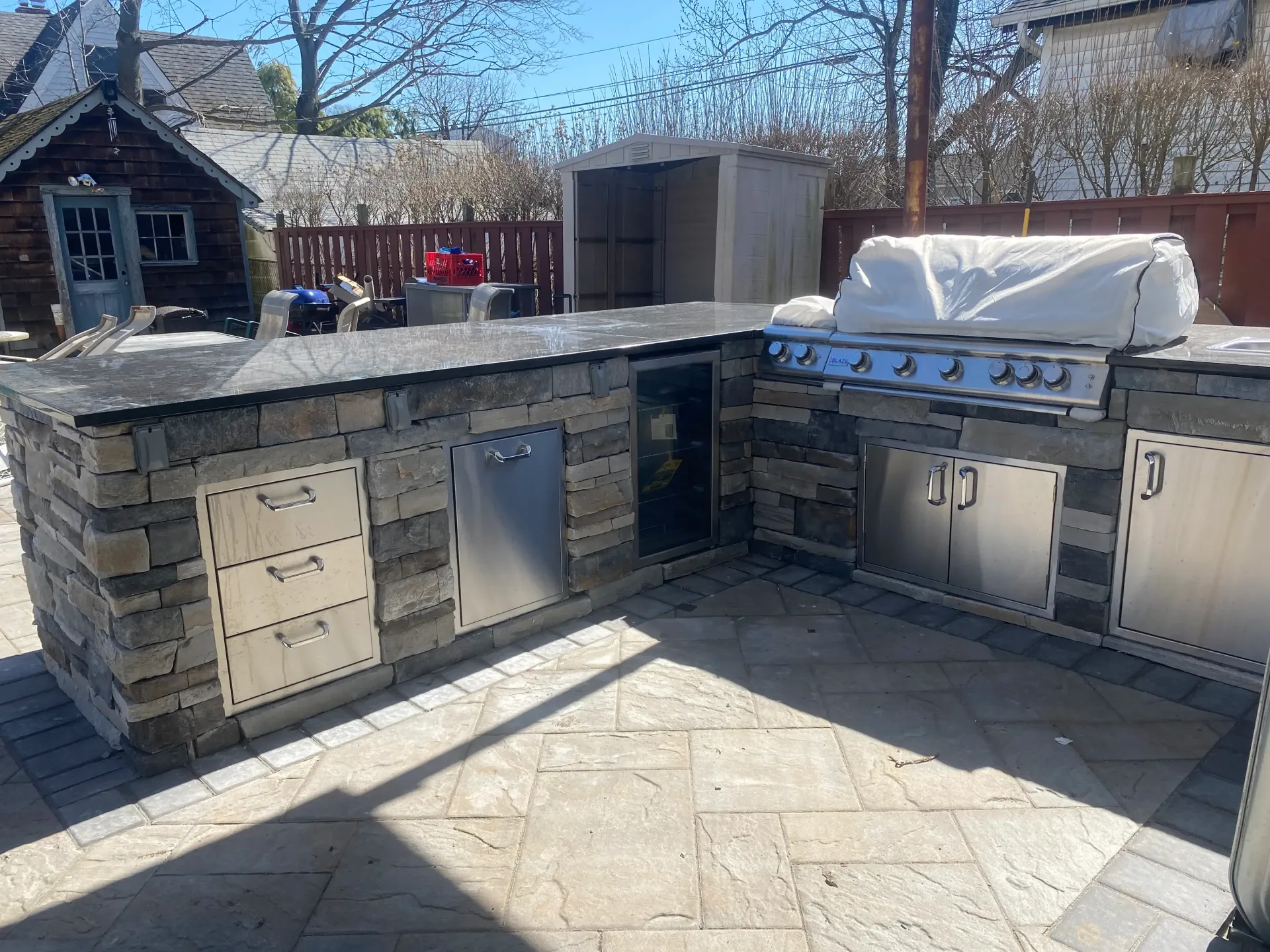 Outdoor kitchen with stone facade, stainless steel appliances, and grill covered.