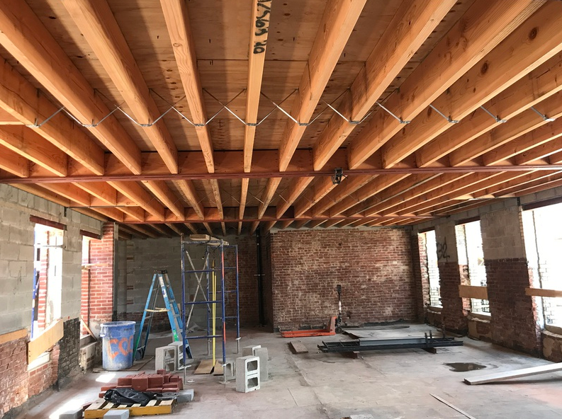 Interior construction site with exposed wooden beams, brick walls, and scaffolding.