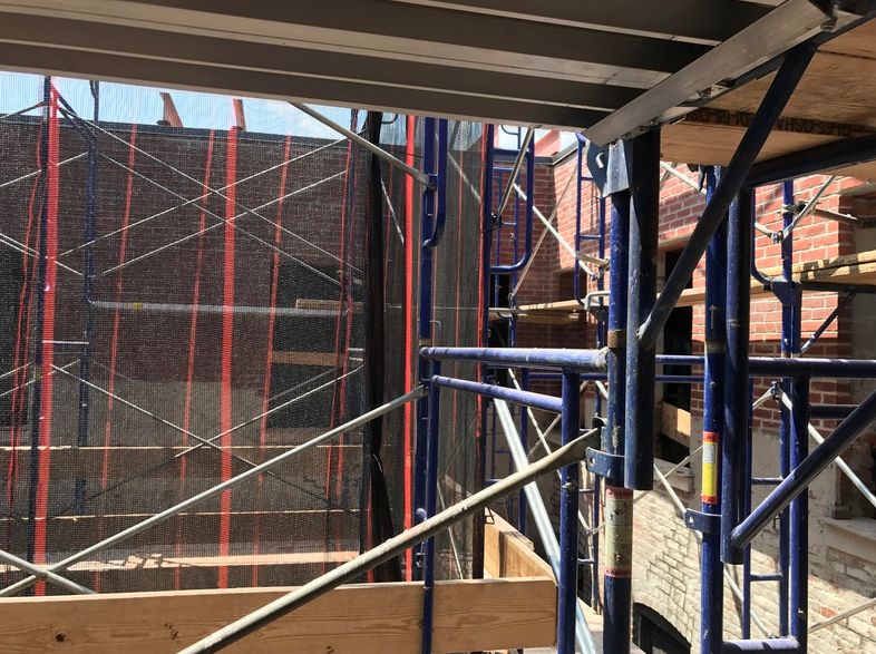 Scaffolding set up in front of a brick building, with safety netting and wooden planks.