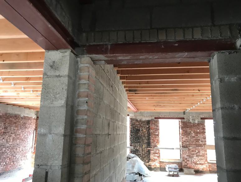 Interior construction site: concrete block walls, brick accents, wood beams, and steel beam.