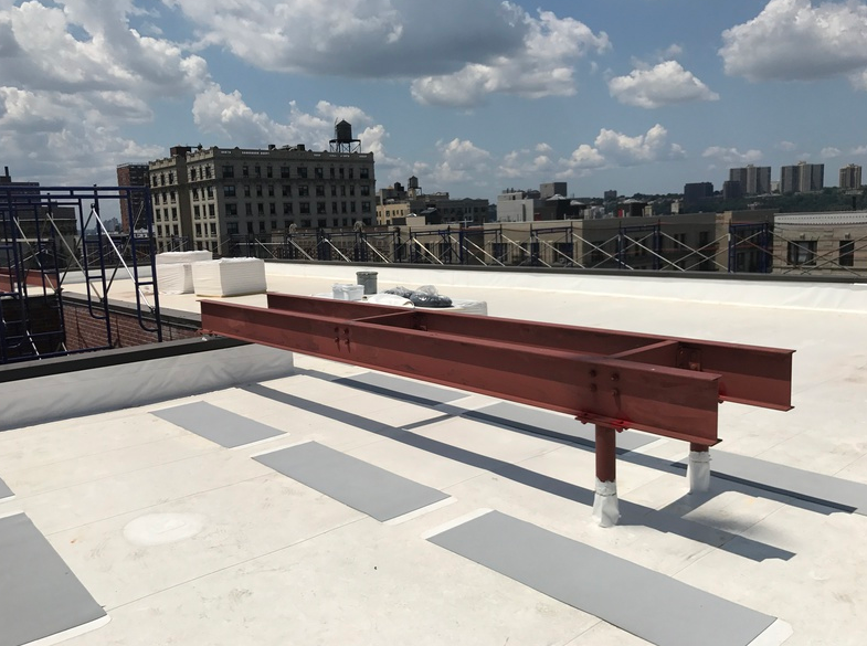 Red metal beams on a white roof. City buildings and blue sky in the background.