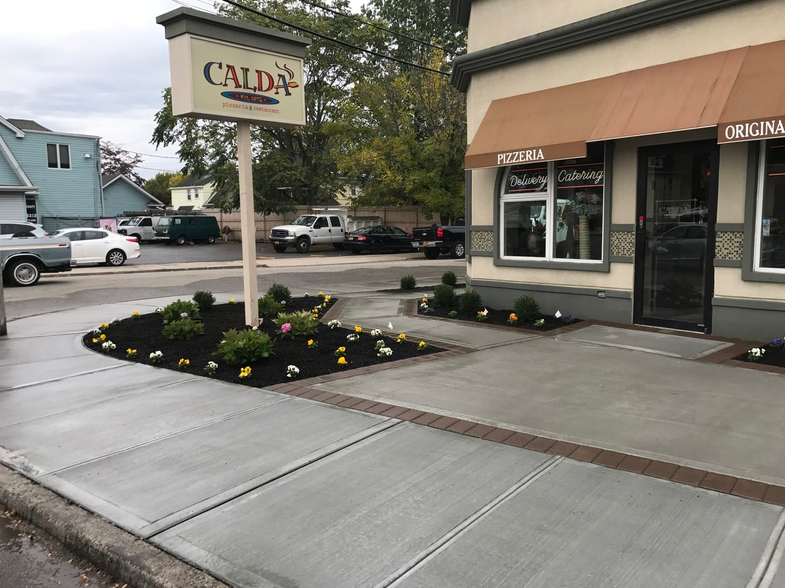 Exterior of Calda's restaurant with a sign. Sidewalk with flower beds and vehicles on the street.