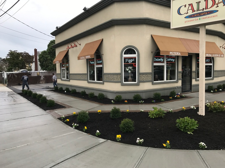 Corner building with beige exterior, brown awnings, and fresh landscaping, with a sign that says