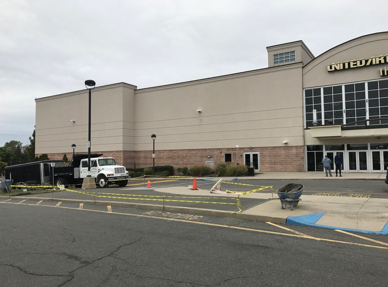 A white truck parked in front of a United Artists movie theater, caution tape and debris on the ground.