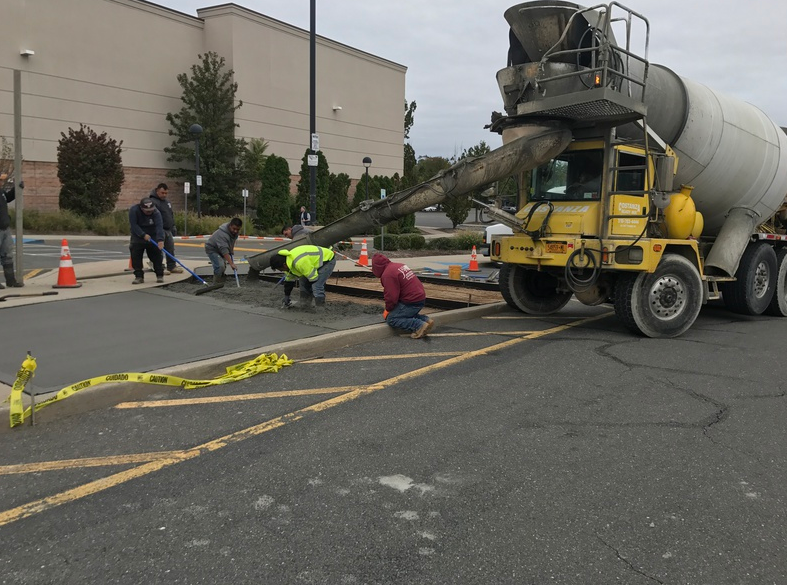 Concrete being poured by a truck onto a parking lot; construction workers are smoothing it.