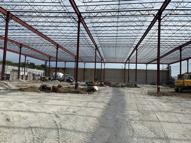 Steel frame of a warehouse under construction, red beams and gray walls, outdoor setting.
