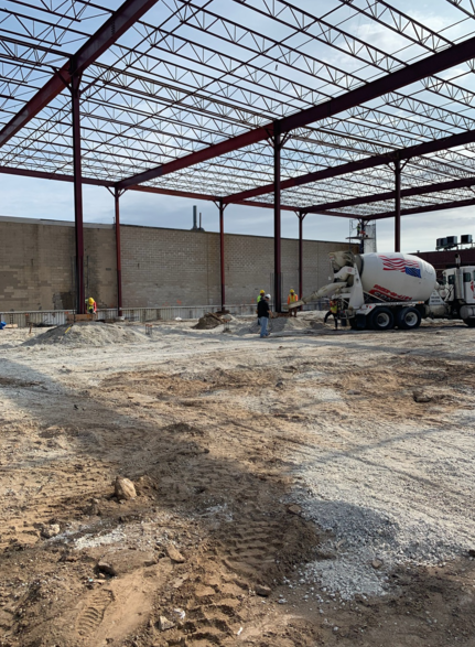 Construction site: steel frame building, concrete truck, workers, dirt and gravel.