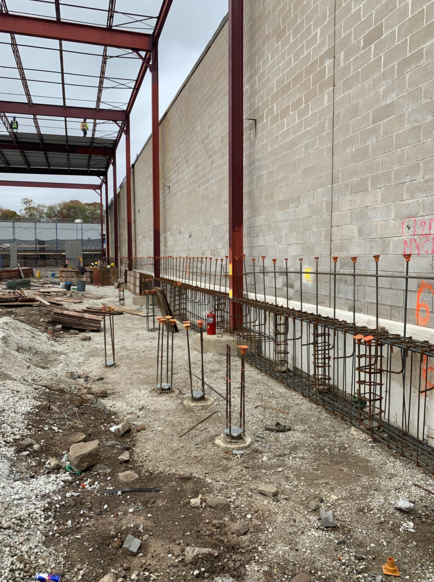 Construction site with steel framework and concrete block wall. Rebar is visible along a low retaining wall.