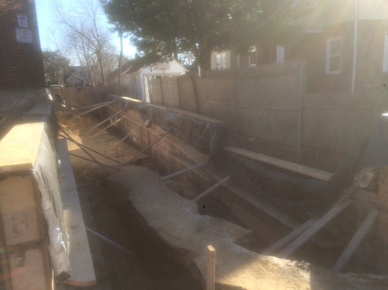 Construction site with wooden forms in a trench, awaiting concrete. Exterior setting, sunny day.