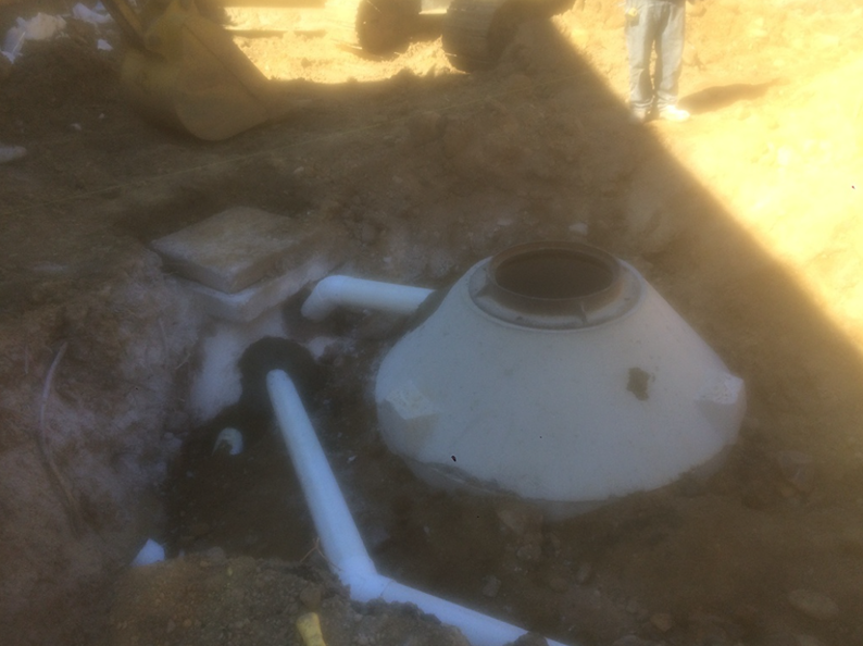 White septic tank installation in a dirt trench, with connected pipes.
