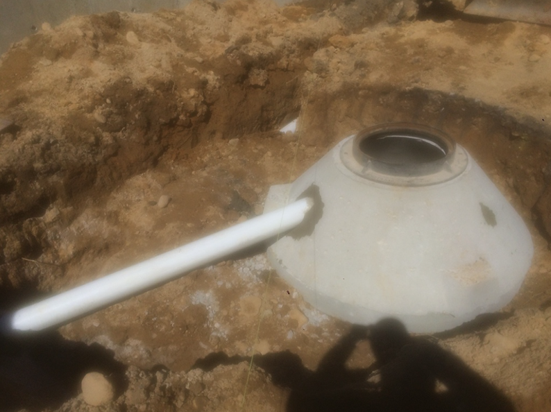 White plastic dome in a sandy hole, with a white pipe extending from its side.