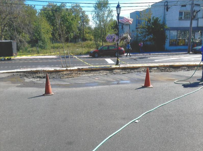 Two orange traffic cones on asphalt near a street with construction. A red car drives by.