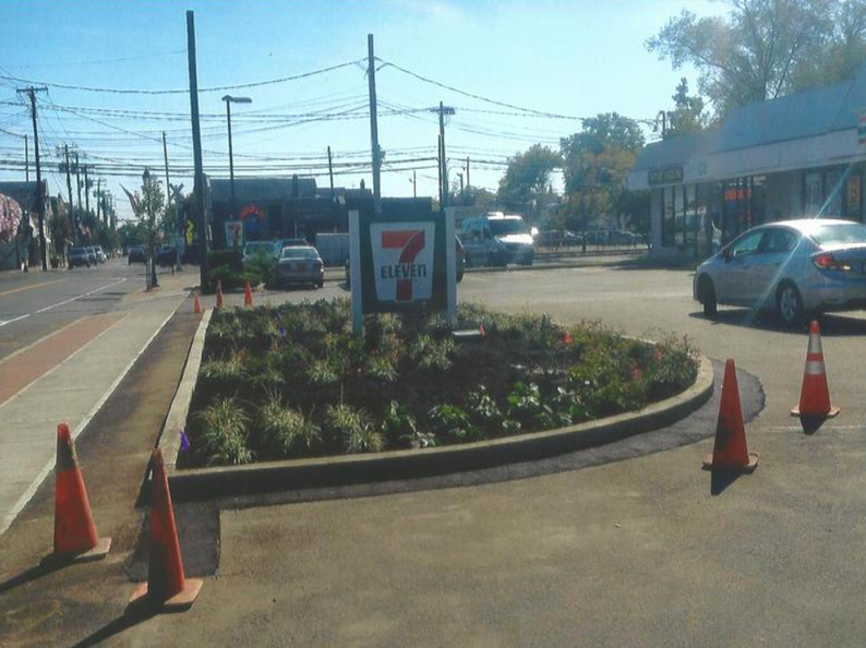 7-Eleven store with landscaping. Cars on road. Orange cones in front of the curb. Sunny day.