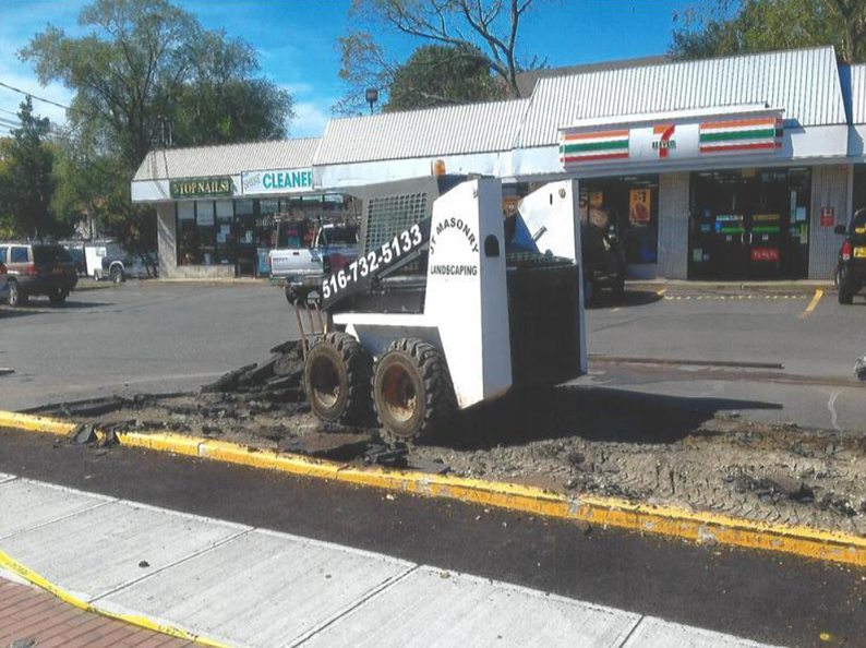 A white Bobcat removes asphalt from a street in front of a 7-Eleven store.