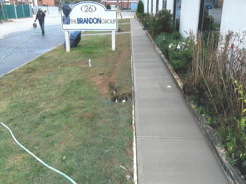 A newly paved sidewalk next to a building and grass, with a sign for The Brandon Group.