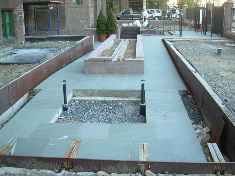 A gray stone walkway with metal borders, featuring rectangular planters and inset fixtures.