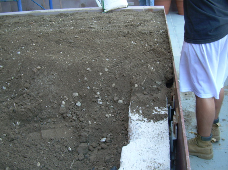 Person adding soil to a raised garden bed, side view.