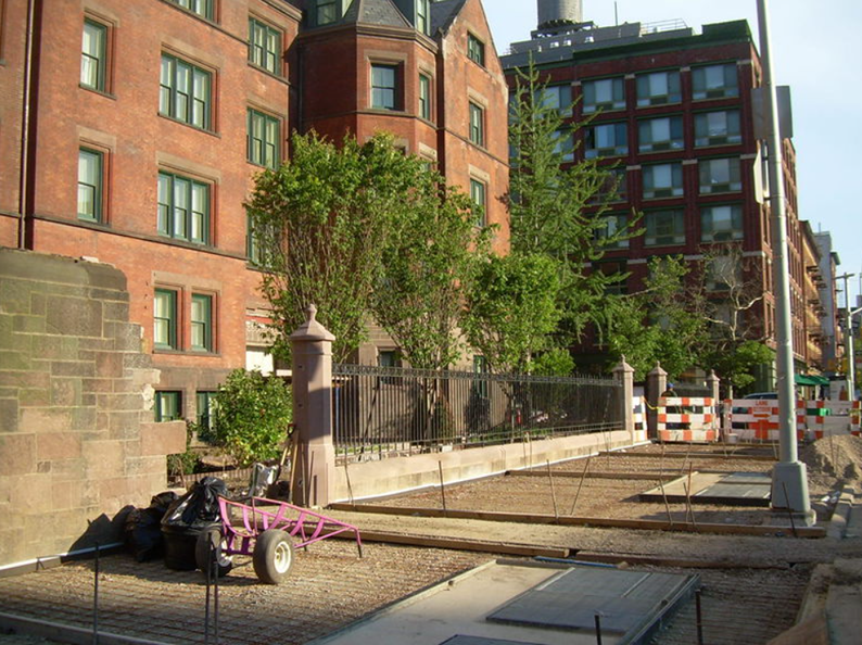 Construction site on a city street; brick buildings, trees, and a machine in the foreground.