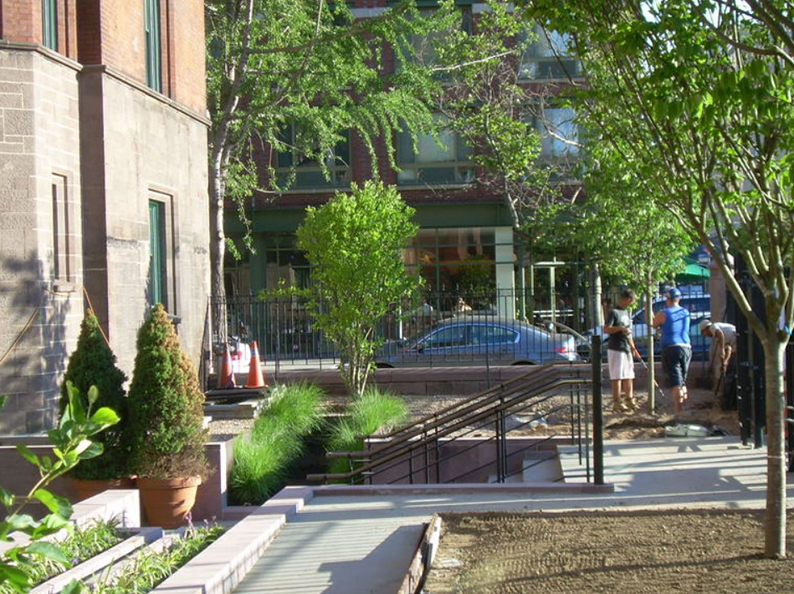 Sidewalk with building and trees, people standing.