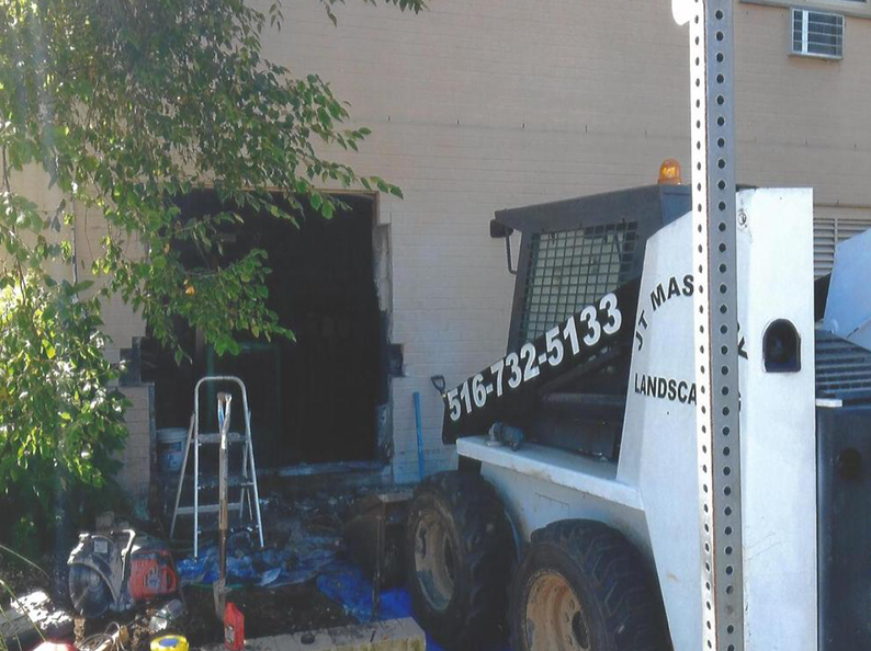 A white and black skid steer by a building with an open doorway. A ladder and equipment are nearby.