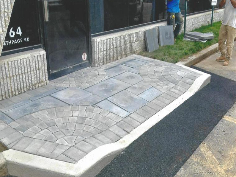 A stone walkway and ramp leading to a building entrance, with workers and building in the background.