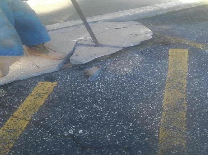 Person breaking concrete sidewalk with a metal tool in a parking lot.