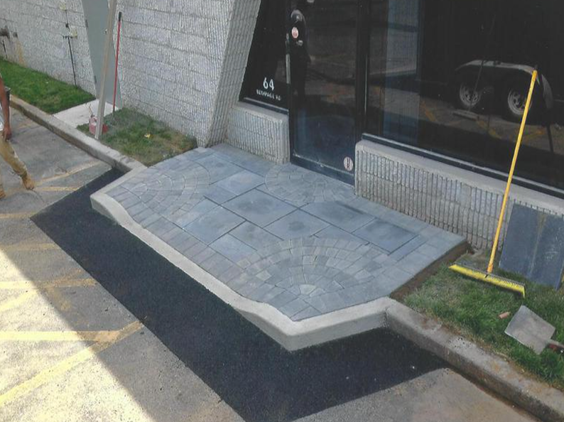 Brick entrance to a building with black asphalt and green grass. A person walks in the background.