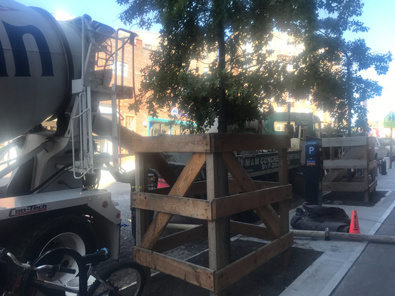 A cement truck and wooden crate on a newly paved sidewalk, with trees and a building in the background.