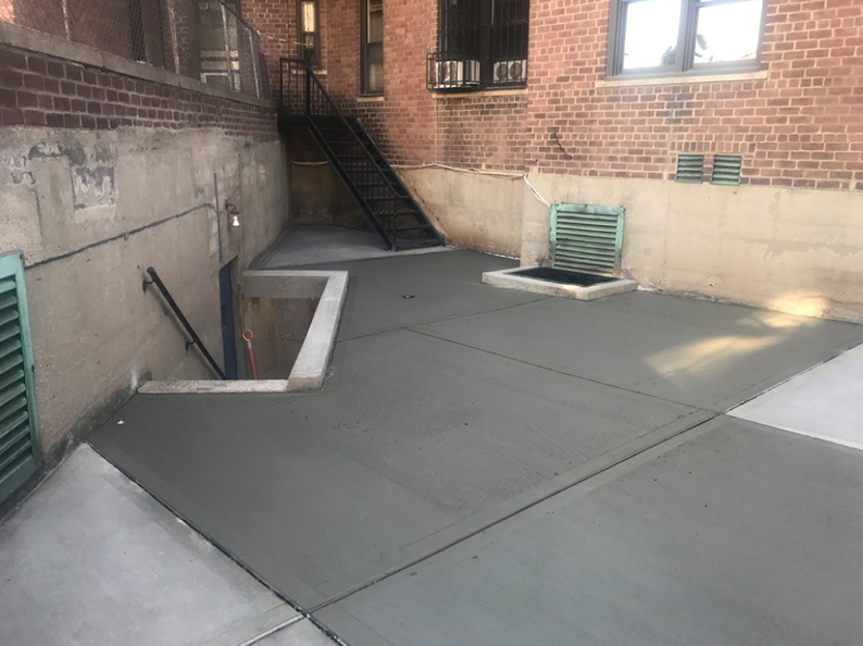 Exterior view of a building with newly poured gray concrete. Entrance, stairs, and vents are visible.