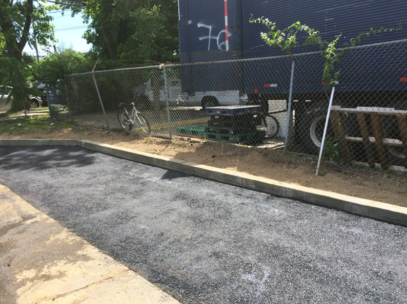Black asphalt pavement, concrete curb, chain link fence, bike, parked near a truck.