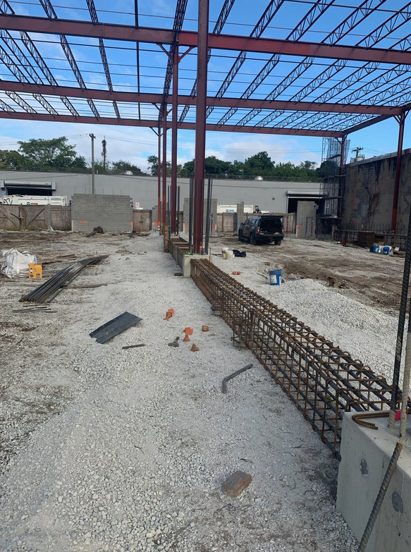 Construction site: steel frame, rebar, gravel, concrete foundation, under blue sky.