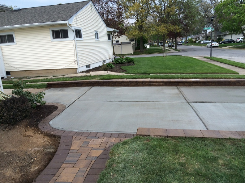Concrete driveway and brick walkway next to a house with green grass and landscaping.