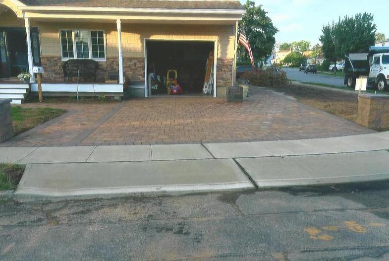 Driveway paved with brick-like stones, leading to an open garage, and a small porch.
