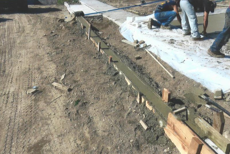 Construction workers pouring cement into a wooden form for a curb.