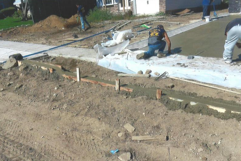 Construction workers laying concrete driveway. Ground-level view, sunny day.