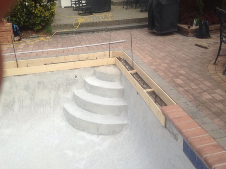 Pool under construction: Concrete steps, wooden forms, brick coping, and rebar along the edge.