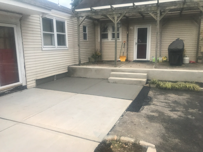 Concrete patio with steps, connecting to a raised covered porch and building.