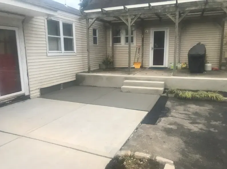 Concrete patio with steps, ramp, and a covered porch.  Building with tan siding.