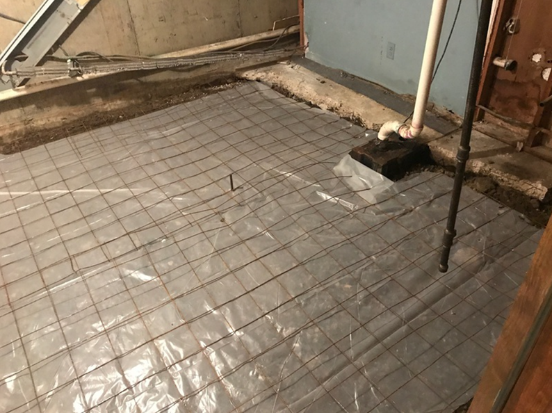 Basement floor construction: plastic sheeting, wire mesh, plumbing visible.