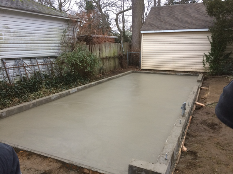 Freshly poured concrete slab with forms, in a backyard setting, ready for construction.
