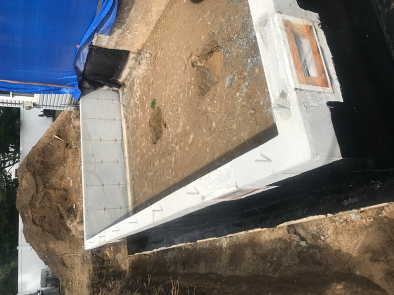 Construction site with white concrete walls and exposed earth. Blue tarp and dirt visible.