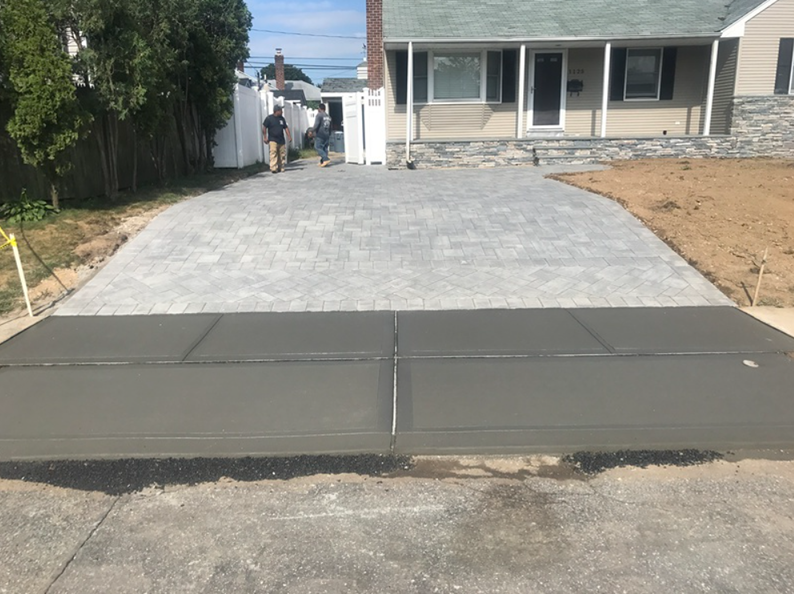 Driveway with freshly poured concrete and pavers, with workers and a house in the background.