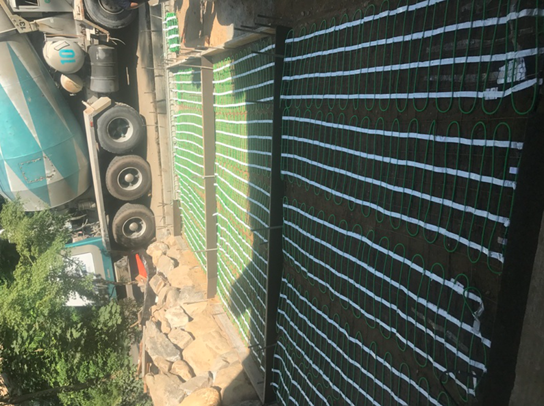 Electric underfloor heating cables laid out before concrete pour near a cement truck.