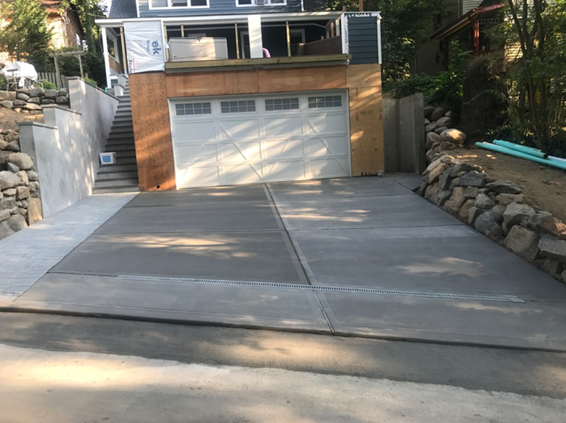 Concrete driveway leading to a garage under a house; retaining walls on both sides.