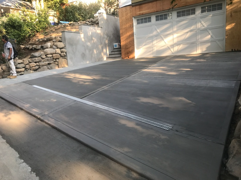 New concrete driveway with a drainage channel, next to a garage. A person stands near.