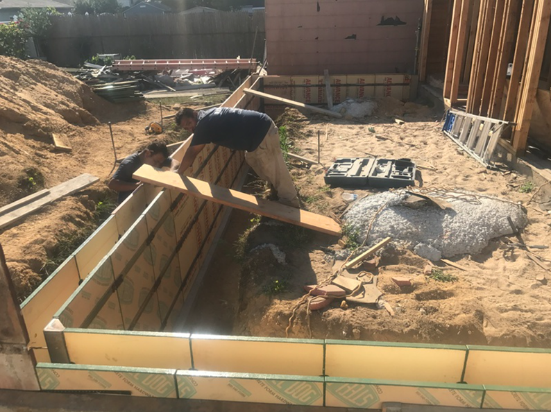 Two construction workers building a foundation for a house, setting boards in the ground.