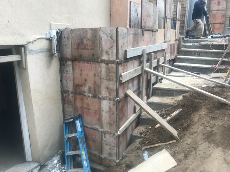 Wooden forms built for concrete construction next to stairs, a building, and a construction worker.